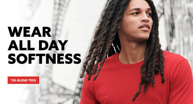Person wearing a red shirt with text 'Wear All Day Softness' and 'Tri-Blend Tees' on a blurred natural background.