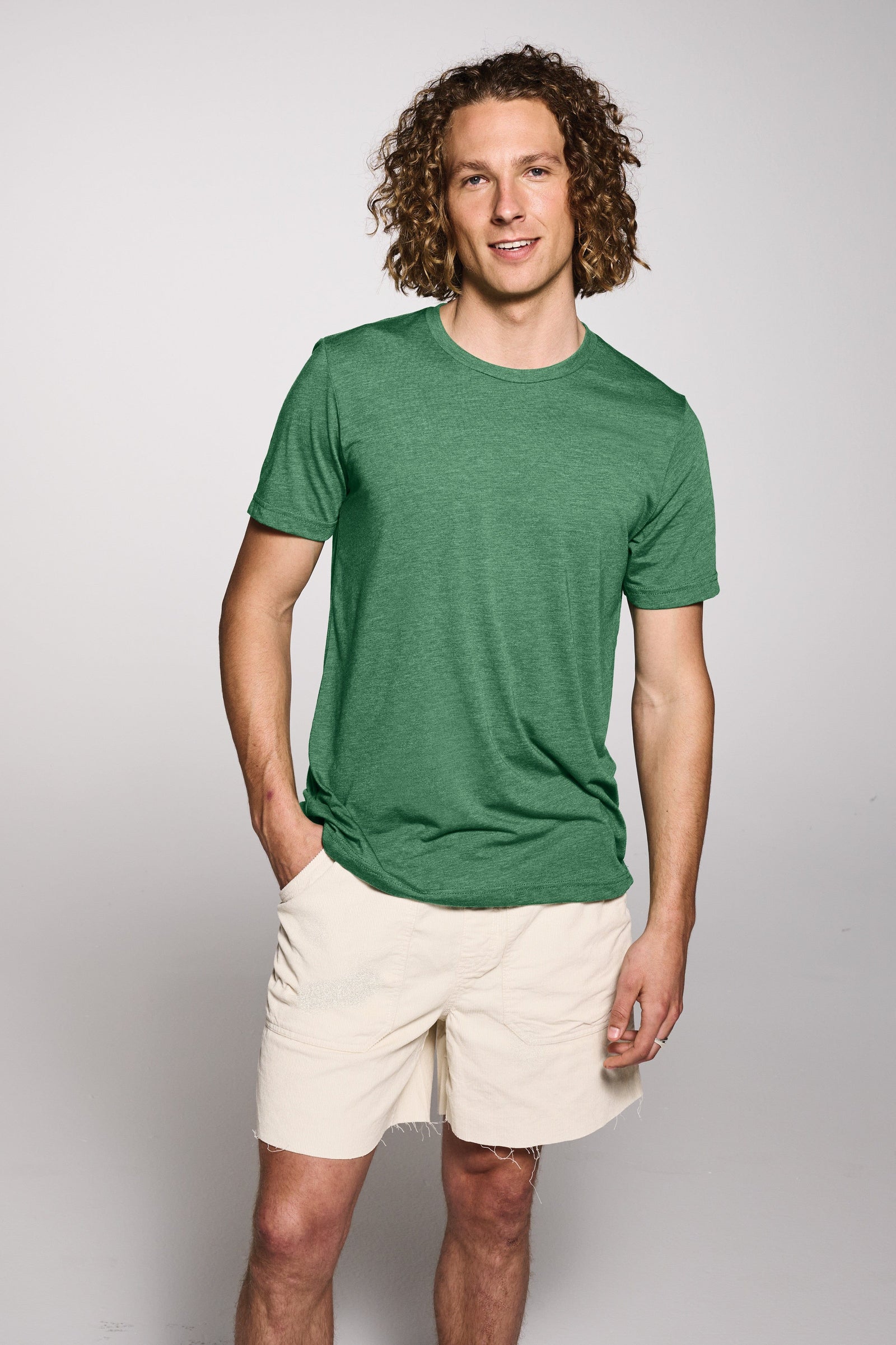 Man wearing a green t-shirt and beige shorts against a plain background
