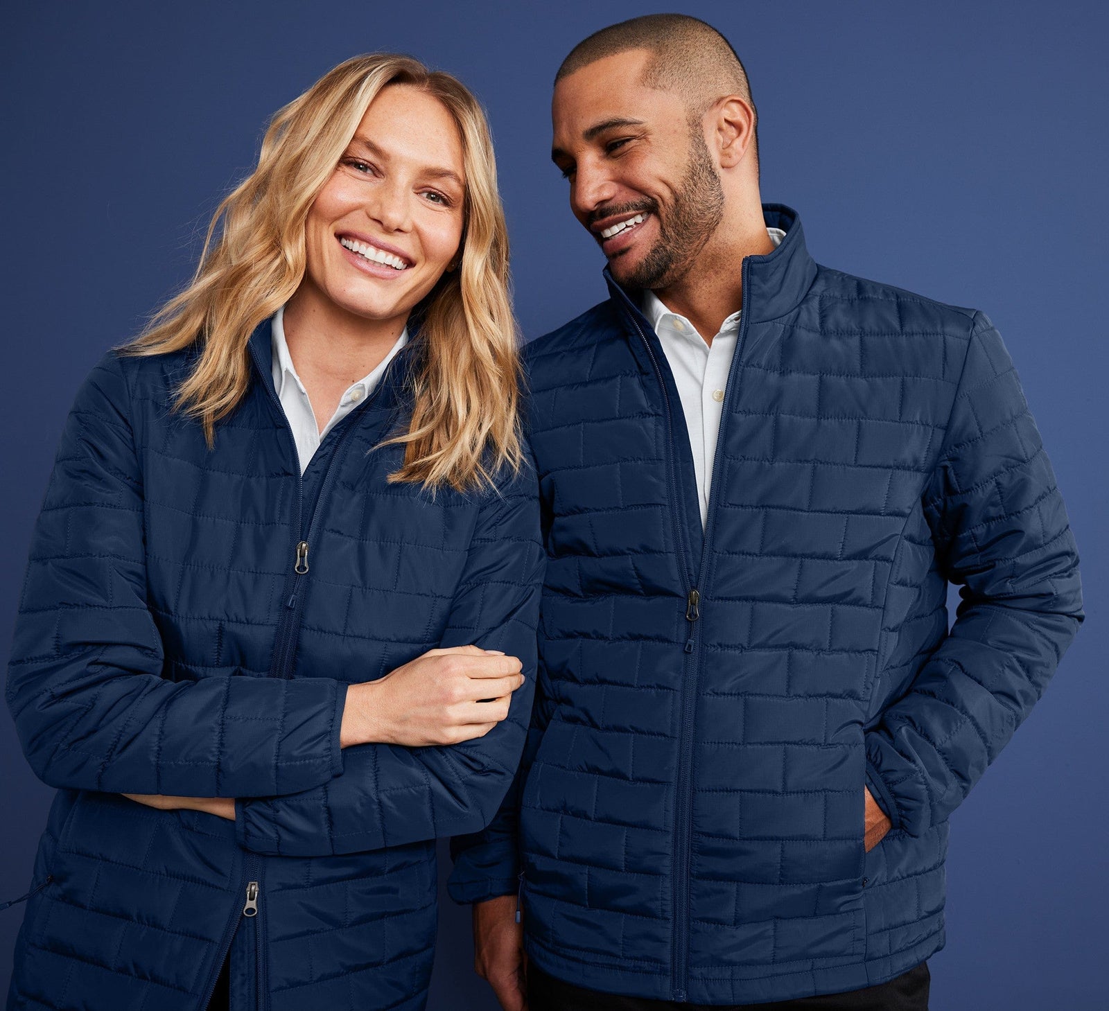 Two people wearing matching blue quilted jackets against a dark blue background