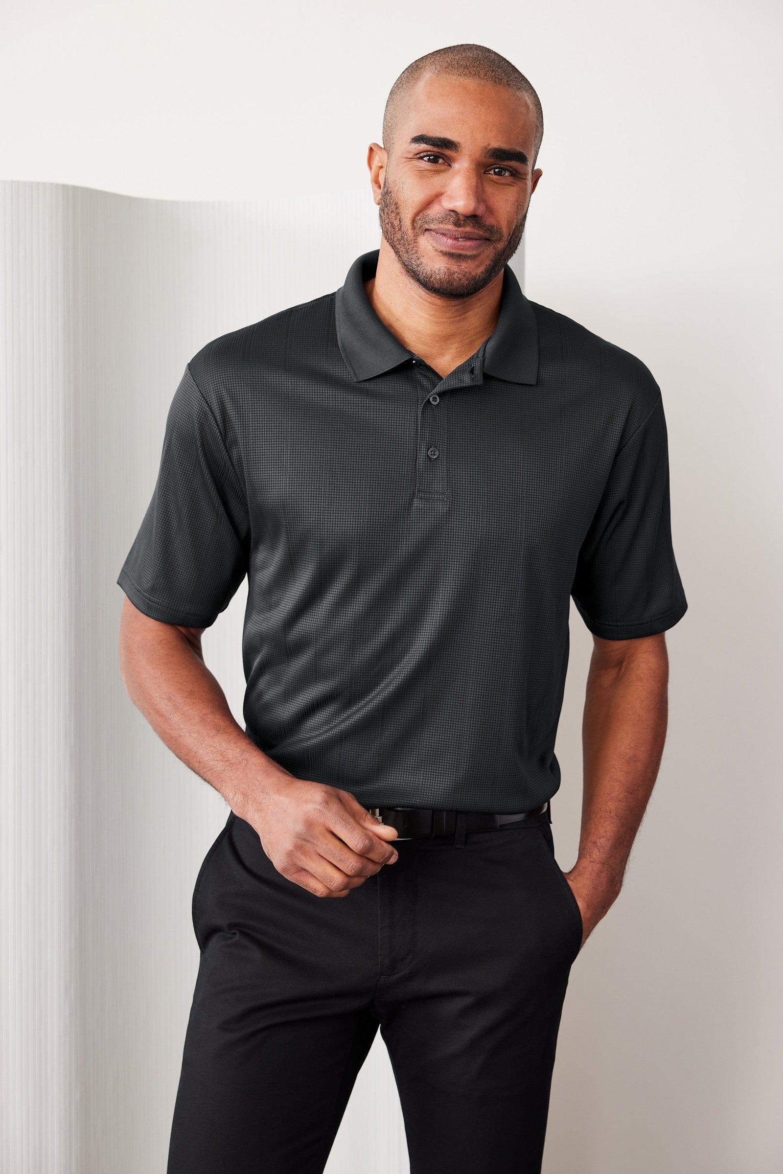 Man wearing a black polo shirt and pants against a plain background